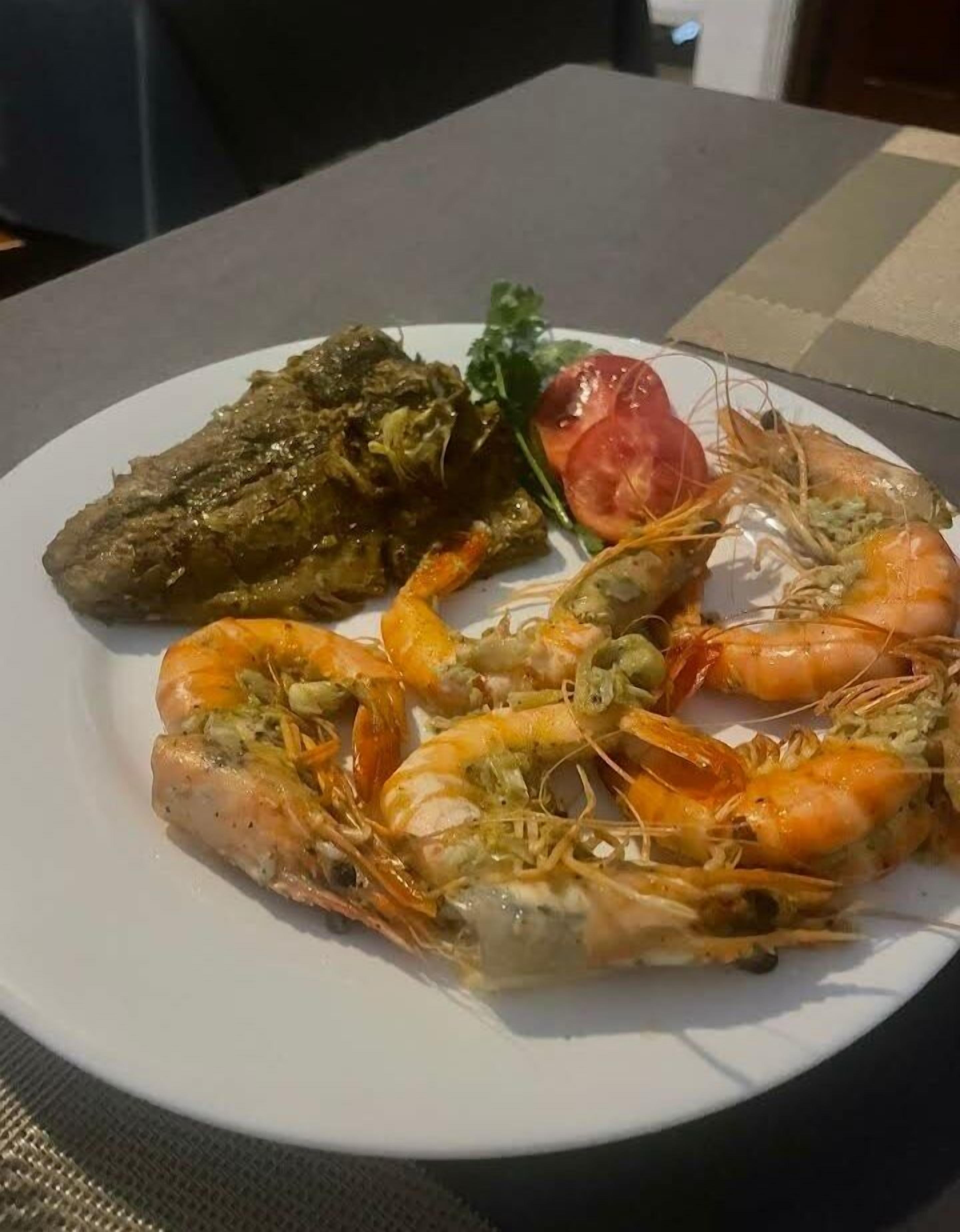 Un plato con camarones cocidos, un trozo de carne y un tomate sobre una mesa.