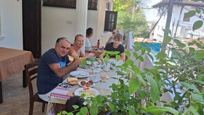 Un grupo de personas cenando en una mesa al aire libre, con varios platos y bebidas.