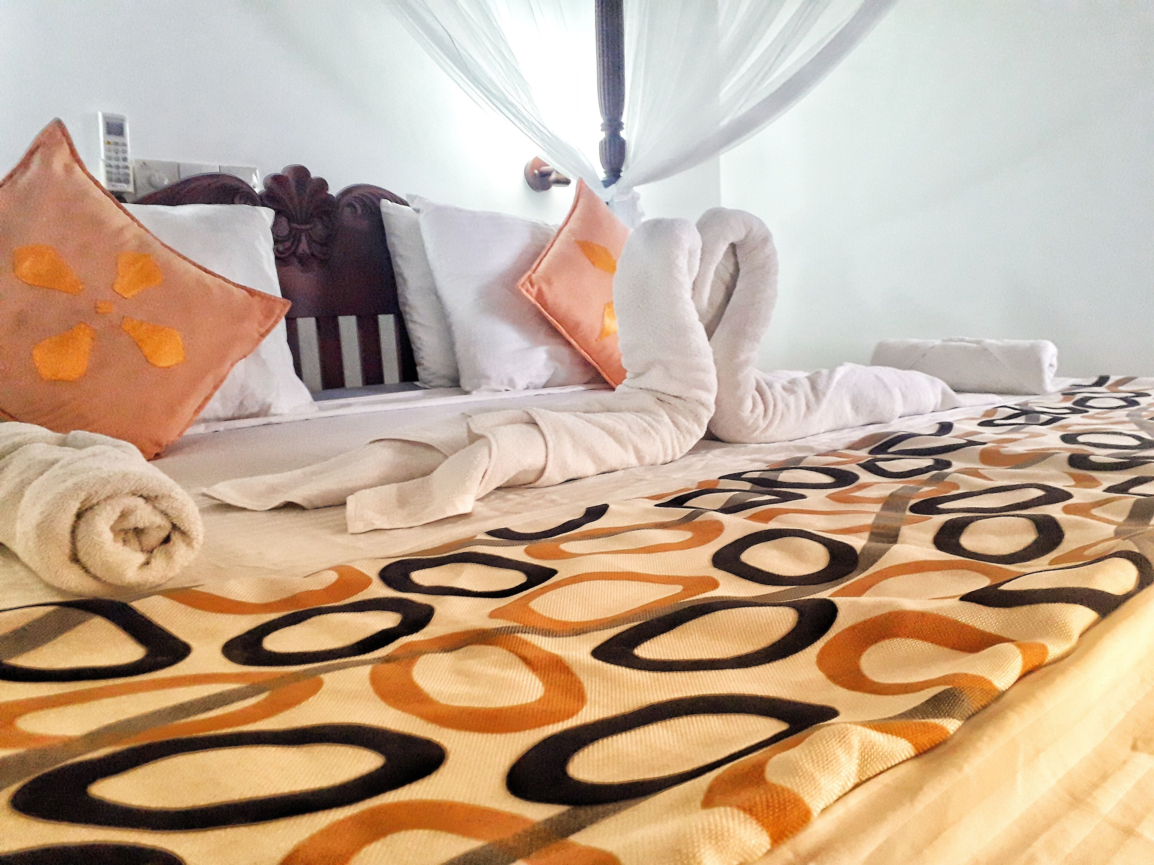 Una cama bien tendida con un edredón estampado, almohadas y una toalla enrollada.