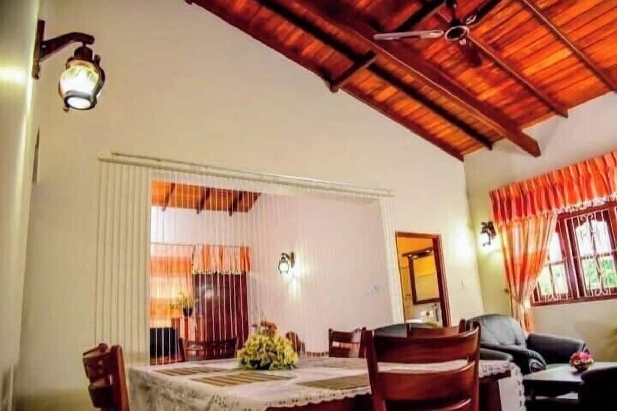 Uma sala de jantar com uma mesa posta para quatro pessoas, rodeada por cadeiras, e um ventilador de teto acima.