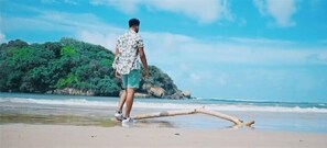 A person walking on a beach with a large log on the sand and a forested island in the background. - Lucky Prince Villa & Ayurveda Wellness (Beruwala)