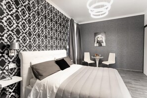 A modern bedroom with a patterned wallpaper, a large bed with a headboard, a bedside table with a lamp, and a small table with chairs. - B&B Notti d'Oriente (Sutri)