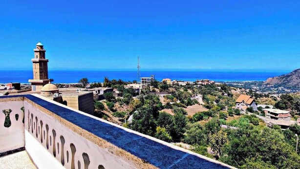 A coastal town with a prominent tower, terraced houses, and a clear view of the sea. - La Résidence Location Daoud (Souk El Tenine)