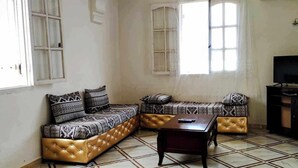 A living room with a sofa set, a coffee table, and a television. - La Résidence Location Daoud (Souk El Tenine)