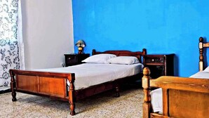 A room with two wooden beds, a nightstand with a lamp, and a patterned curtain. - La Résidence Location Daoud (Souk El Tenine)
