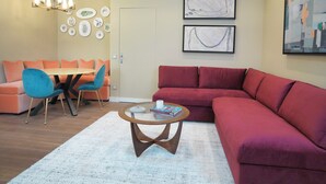 A modern living room with a red sofa, blue chairs, a round coffee table, and a chandelier.