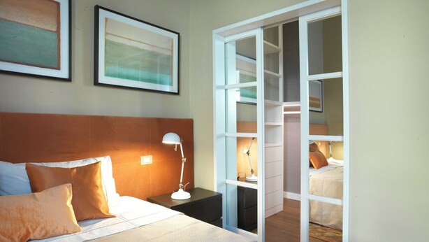 A hotel room with a bed, bedside table, lamp, and a wardrobe with a mirror.