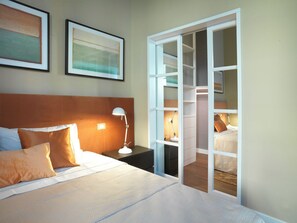 Habitación de hotel con cama, mesita de noche, lámpara y un armario con espejo.