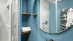 A bathroom with a glass shower enclosure, a round mirror, and a towel rack.