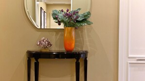 A room with a round mirror on the wall, a black console table with a vase of flowers, and a patterned rug on the floor.