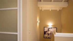 A narrow hallway with a staircase, a framed artwork on the wall, and a light fixture above it.