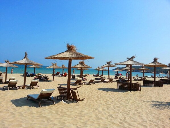 Relax on comfortable sun loungers under shaded thatched umbrellas with a view of the ocean.
