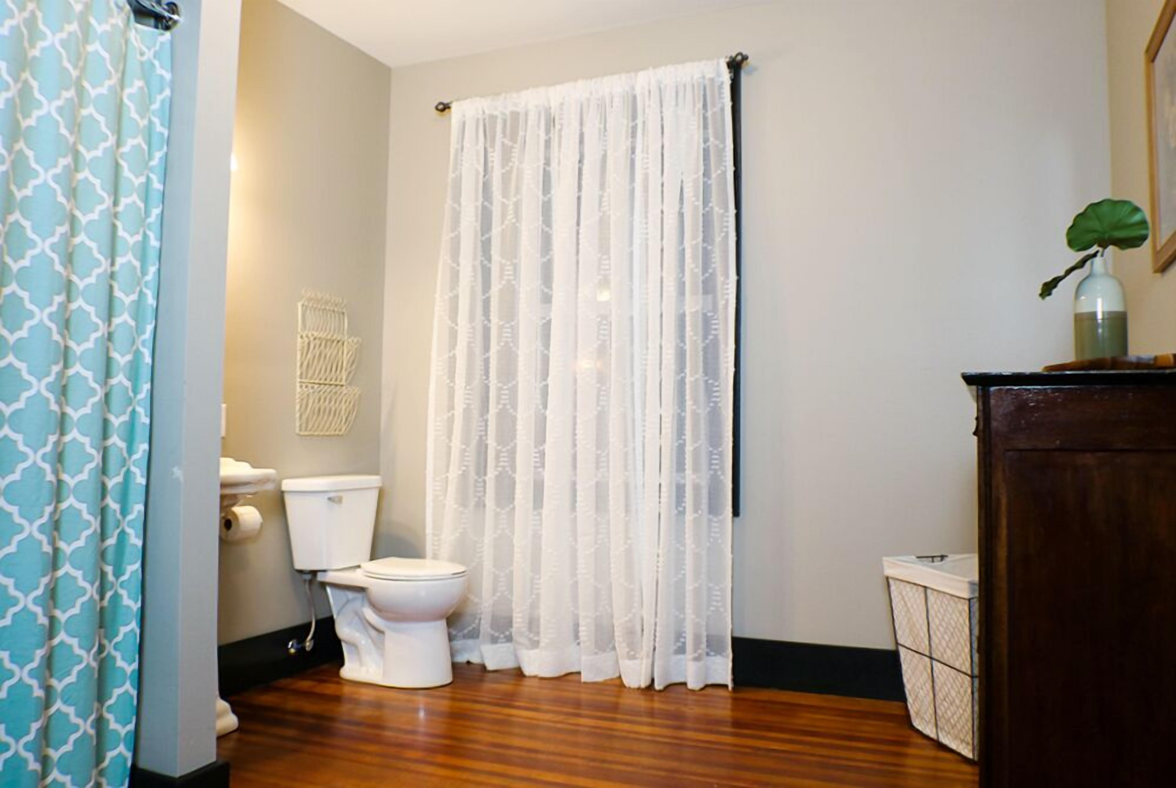 A bathroom with a toilet, a shower curtain, and a wooden floor.
