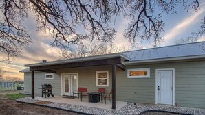 A single-story house with a covered patio, a barbecue grill, and two red chairs.
