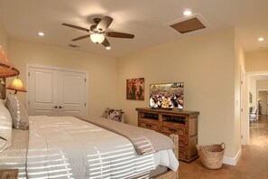Un dormitorio con cama, ventilador de techo, televisor y aparador de madera.