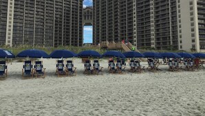 Una zona spiaggia con file di sdraio e ombrelloni, una scala che conduce a un edificio e un grande edificio sullo sfondo.