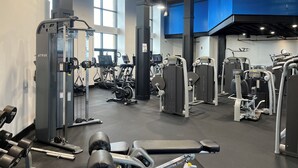 Una palestra con diverse macchine per esercizi, attrezzature per sollevamento pesi e ampie finestre che lasciano entrare la luce naturale.
