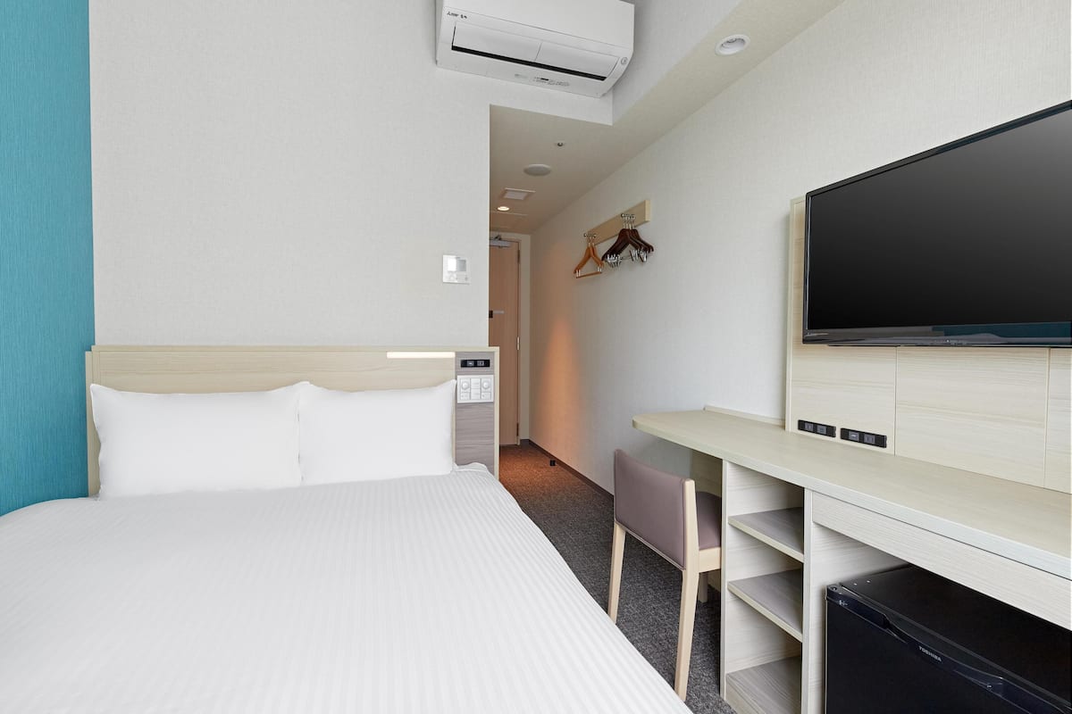 A hotel room with a bed, a desk, a chair, a television, and a wardrobe.
