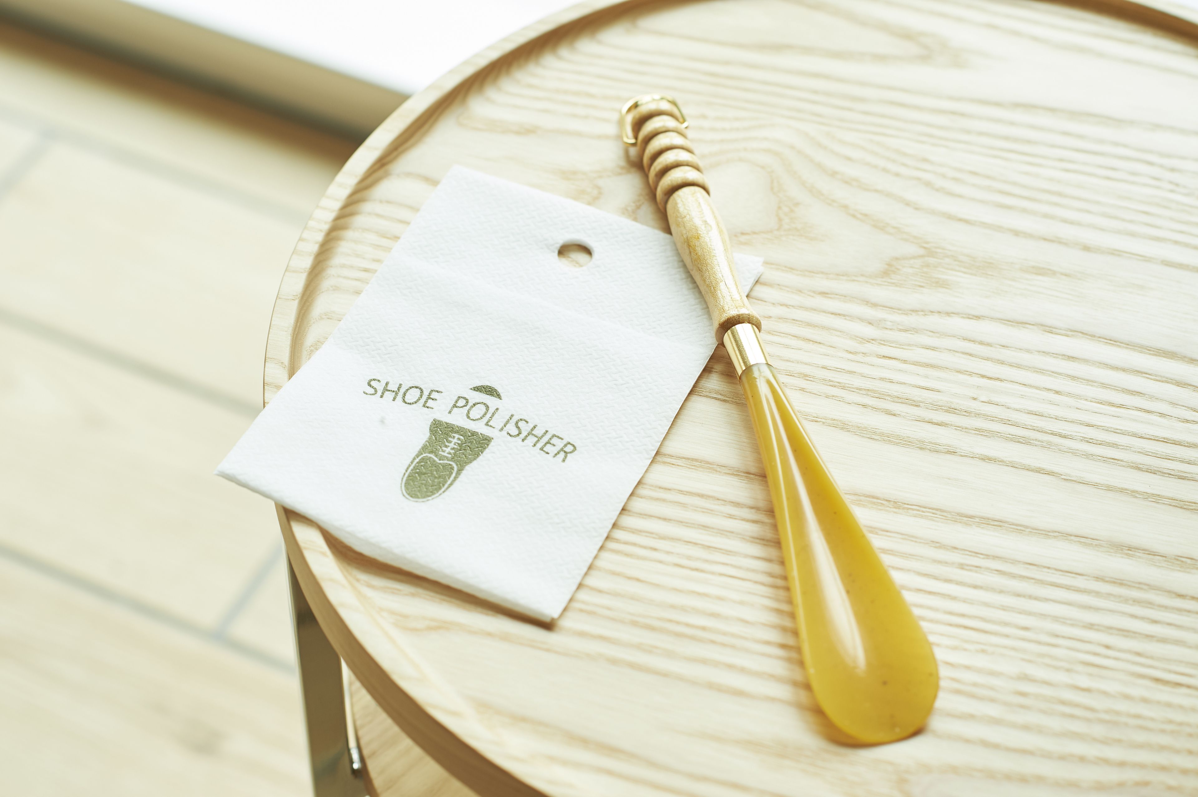 A wooden table with a white tag labeled "SHOE POLISHER" and a yellow polishing brush.