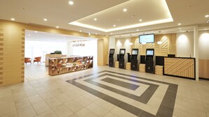 A modern reception area with a check-in counter, self-service kiosks, and a seating area with chairs and a table. - Sotetsu Fresa Inn Osaka-Namba (Osaka)