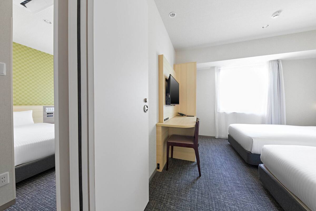 A hotel room with two beds, a desk, a chair, a TV, and a window with curtains.
