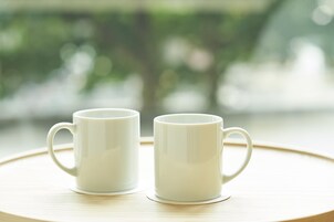 Dos tazas blancas de cerámica sobre una bandeja redonda de madera.