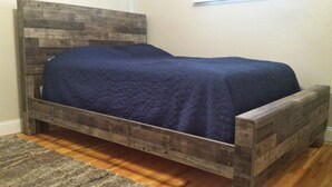 A wooden bed with a dark blue quilt in a room with a wooden floor and a gray rug. - Charming and comfortable home away from home (Rapid City)