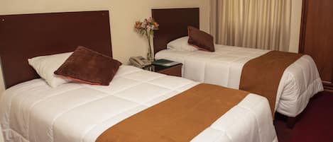 Habitación de hotel con dos camas, cada una con una manta marrón, ropa de cama blanca y una mesita de noche con un teléfono y un florero.