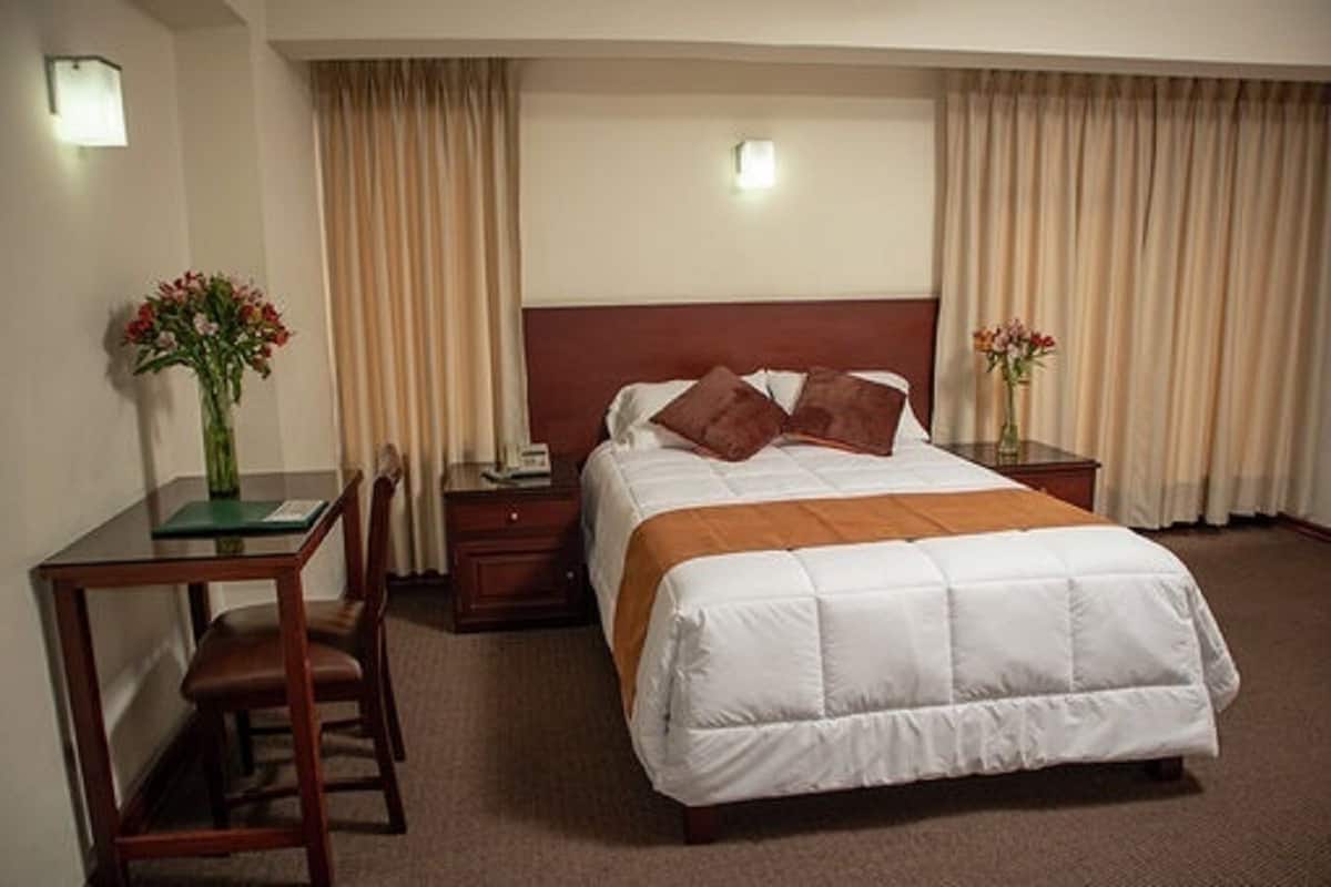A hotel room with a bed, a desk, a chair, and two nightstands.