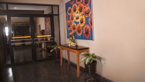 Eine Lobby mit Glastür, einem Holztisch mit Blumenvase und einem großen Blumenbild an der Wand.
