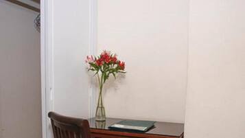 A small office space with a wooden chair, a desk, and a vase with flowers.