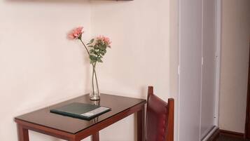 Habitación de hotel con una televisión de pantalla plana montada en la pared, un pequeño escritorio de madera con un florero y una silla de cuero rojo.