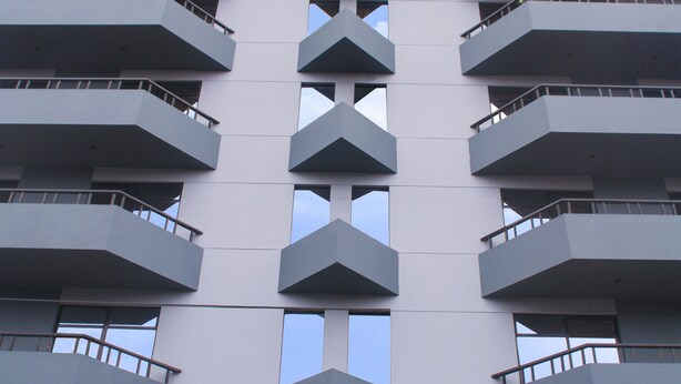 Ein mehrstöckiges Gebäude mit modernem architektonischen Design, das Balkone auf jeder Etage und einen zentralen Eingang mit Stufen aufweist.
