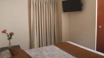 Una habitación de hotel con una cama, un televisor montado en la pared y una cortina.