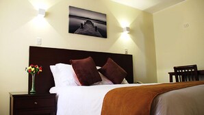 Ein Hotelzimmer mit einem Bett, einem Nachttisch mit Blumenvase und einem an der Wand hängenden Bild.