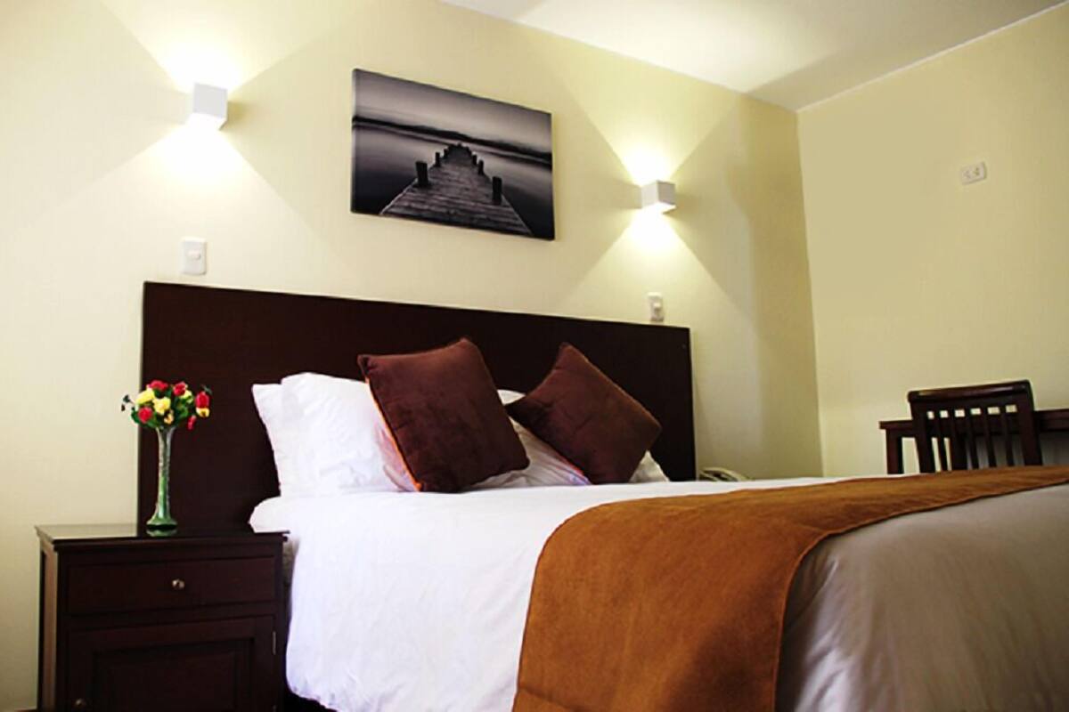 A hotel room with a bed, a nightstand with a vase of flowers, and a wall-mounted picture.