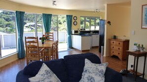 A cozy living room with a dark blue sofa, a dining area with wooden chairs and a table, a kitchen with a refrigerator and microwave, and large windows with curtains. - Jewel in Tata Beach. (Tata Beach)
