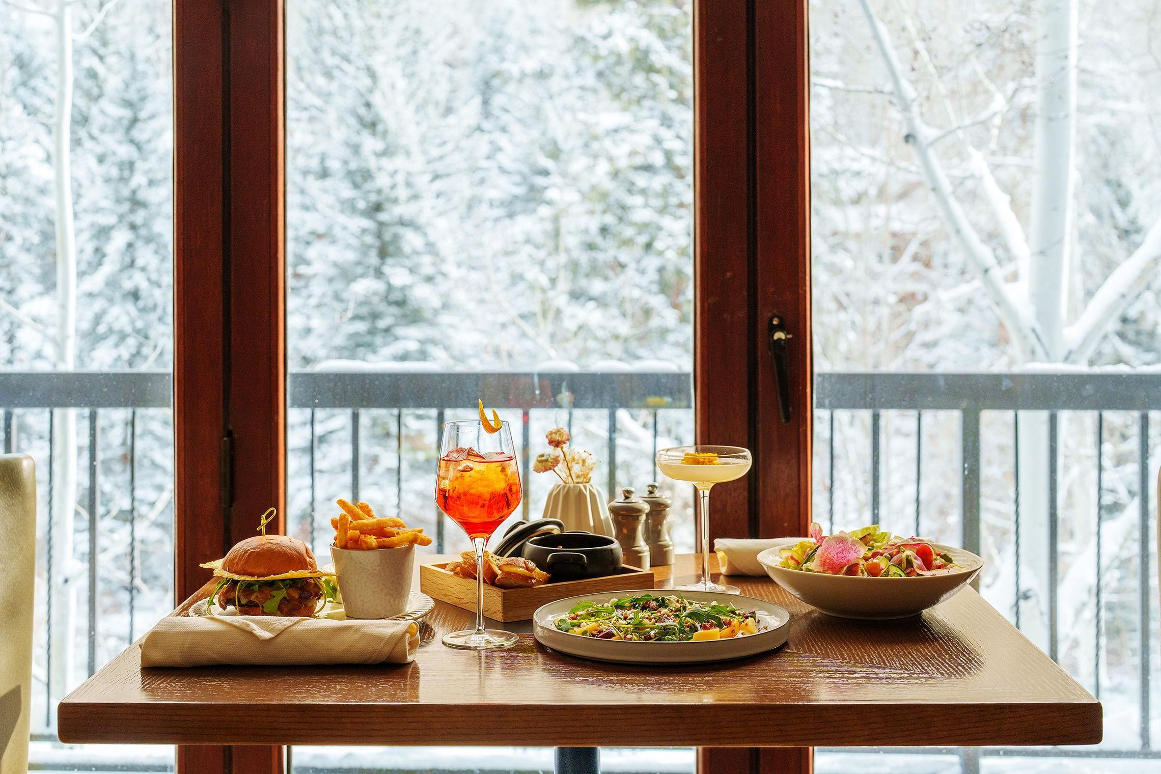 Ett matbord med mat och dryck på en balkong med utsikt över ett snötäckt landskap.