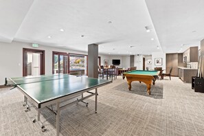 Amplia zona recreativa interior con mesa de ping pong, mesa de billar y zona de estar.