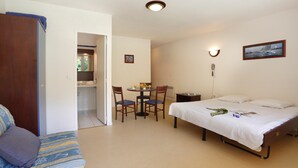 A bedroom with a bed, a desk, and a chair. There is a door leading to a bathroom and a kitchenette.
