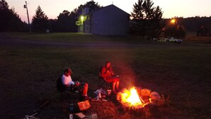 Two people sitting by a campfire in a grassy field with a house in the background. - 14 - Clean, Comfortable and Quiet Condo at the base of Jackson Creek Summit (Wakefield)