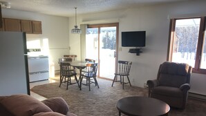 A living room with a brown sofa, a round coffee table, a television on the wall, and a dining area with a table and chairs. - 14 - Clean, Comfortable and Quiet Condo at the base of Jackson Creek Summit (Wakefield)