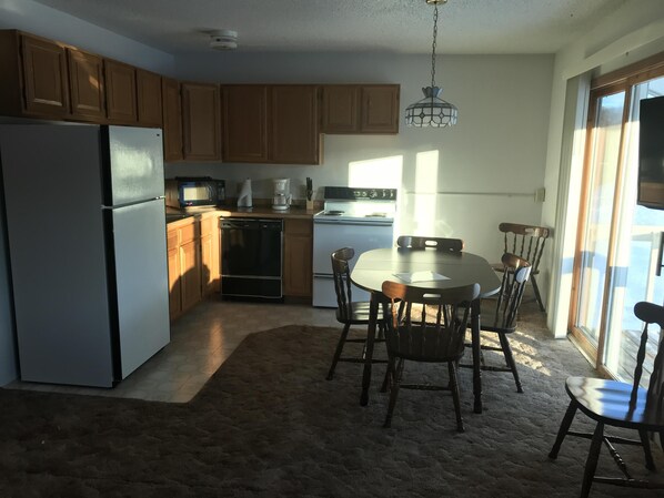 A kitchen with wooden cabinets, a refrigerator, a dishwasher, a stove, and a dining table with chairs.