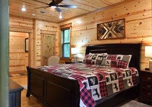 A wooden cabin bedroom with a bed, a ceiling fan, a window, and a door. - Spacious 3600 sq ft 5 king bedrooms with extra bunkbeds (Broken Bow)