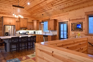 Une cuisine de style rustique avec des meubles en bois, un îlot central doté de tabourets, un réfrigérateur en acier inoxydable et un four encastré.