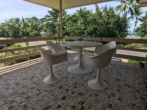 A covered outdoor seating area with a mosaic-tiled floor, surrounded by greenery and palm trees.