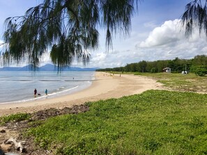 A beach with a clear view of the sea, a sandy shore, and a grassy area with trees.