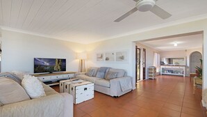 Ein geräumiges Wohnzimmer mit Flachbildfernseher, einer Sofagarnitur, einem Couchtisch und einem Deckenventilator.