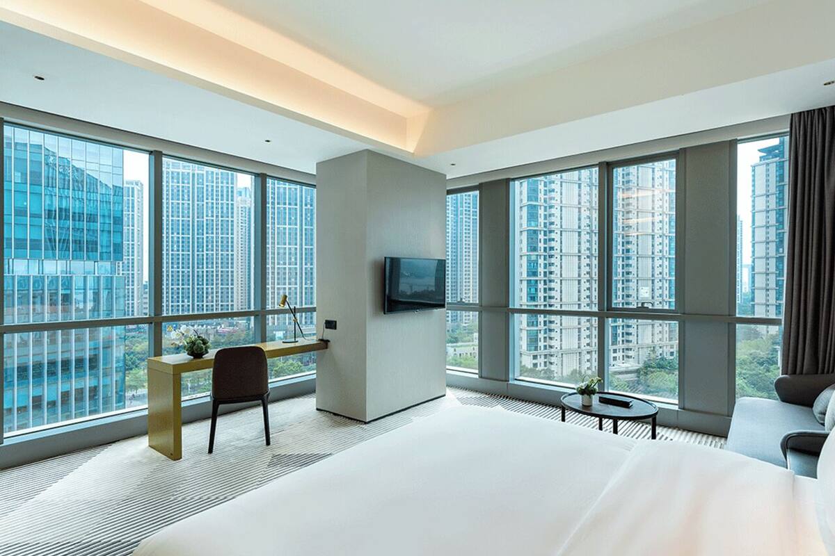 Une chambre d’hôtel moderne dotée de grandes fenêtres, d’un téléviseur à écran plat, d’un bureau et d’un lit confortable.