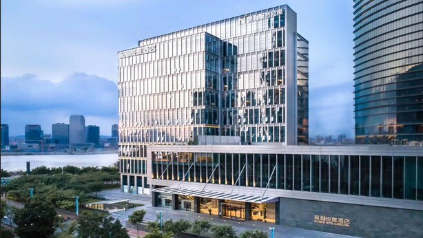 A modern hotel with a glass facade, a covered entrance, and a view of the city skyline. - La Yarda Hotel Guangzhou - Free Shuttle Bus Available during Canton Fair Period (Guangzhou)